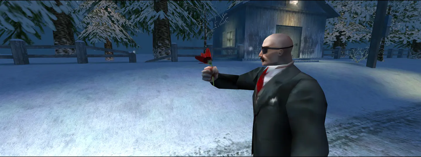 A bald man in sunglasses and a dark suit holds out a red flower in front of a snowy cabin at night.